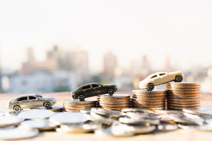 Miniaturas de carros sobre moedas espalhadas numa mesa. Explicando como economizar no seguro auto.