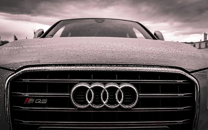 Foco em símbolo da Audi na frente de veículo. Respondendo: audi ou volvo qual oferece mais itens de seguranca no seguro.