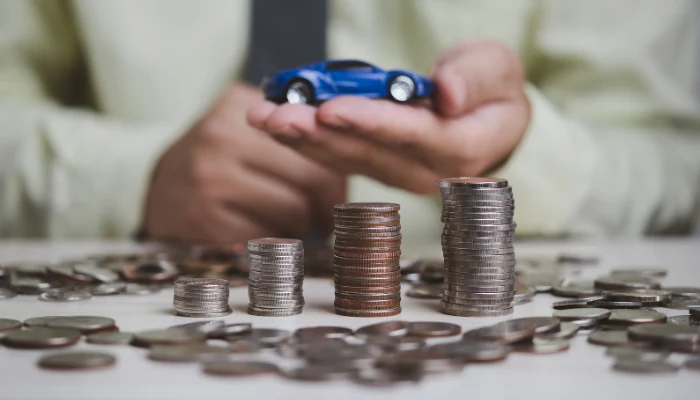 Uma mesa com moedas empilhadas diante da palma de um homem segurando um carro para representar a palavra-chave comparativo de preço.