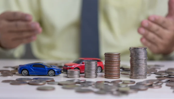 Uma mesa onde várias pilhas de moedas, em diferentes tamanhos, estão acompanhadas de dois carrinhos de brinquedo para representar a palavra-chave economizar seguro audi.