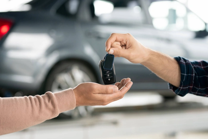 Pessoas trocam chaves de um carro. Ao fundo está o referido veículo. Falando sobre tabela de consórcio de carros.