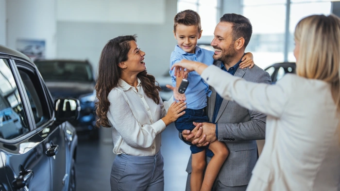 Casal feliz com filho vai até agência buscar carro novo. Corretora dá apoio. Explicando se consórcio de carro vale a pena.
