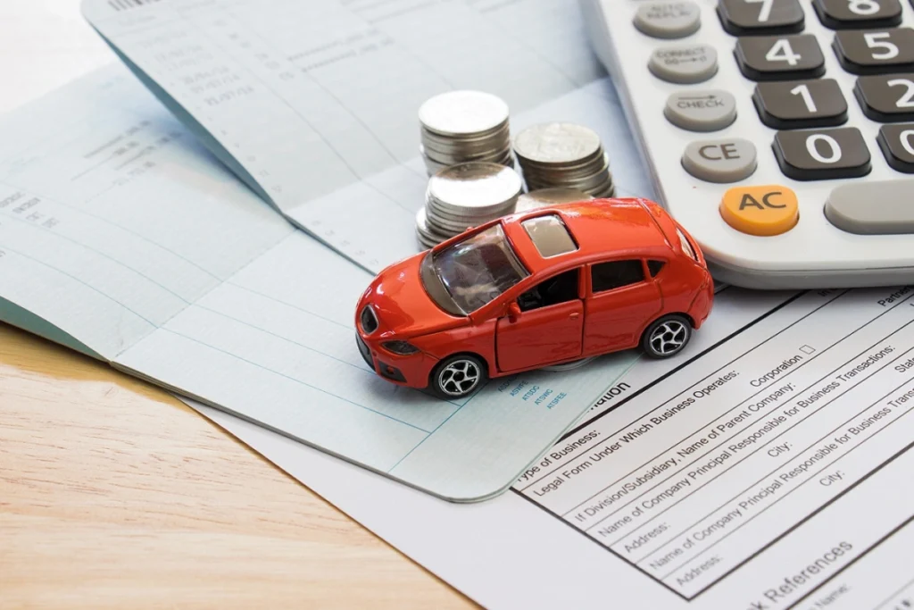 Miniatura de carro vermelho junto a pilhas de moedas, uma calculadora e alguns papéis. Explicando como fazer um consórcio de carros.