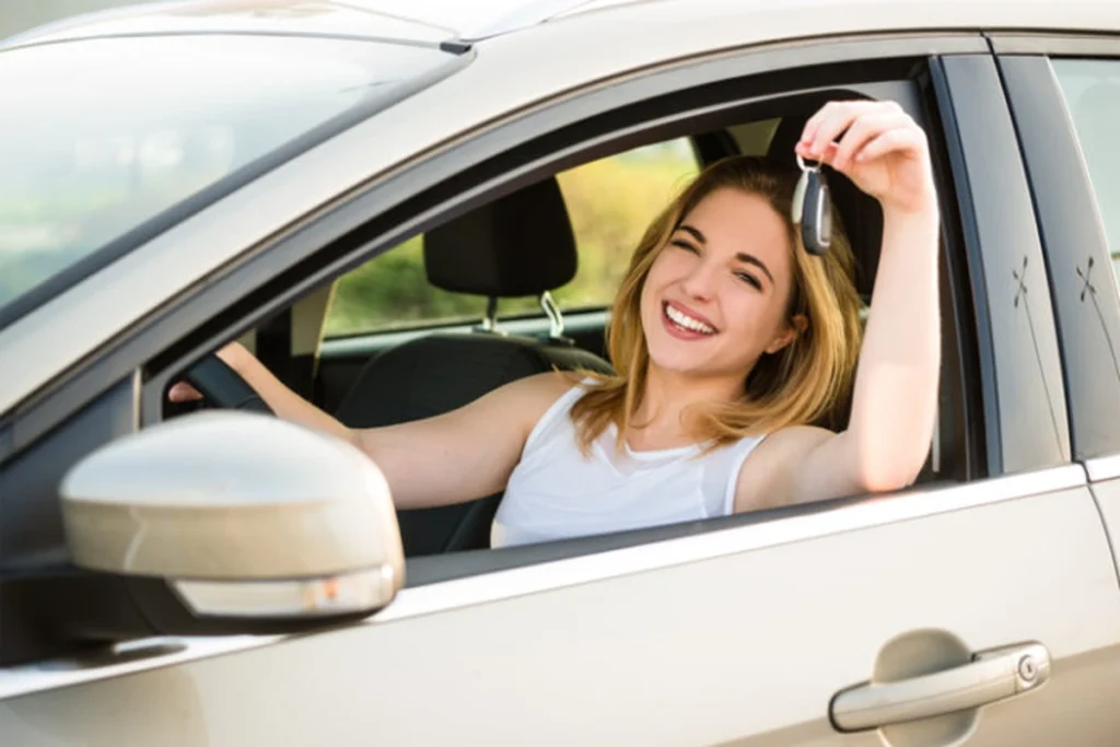 Mulher sorridente exibe chaves de carro enquanto está no interior do veículo. Explicando se consórcio de carro vale a pena.