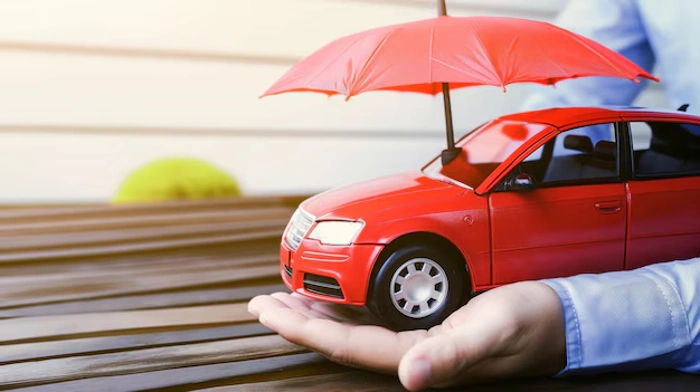 Pessoa segura miniatura de carro vermelho com as mãos e com a outra um mini guarda-chuvas. Falando sobre como escolher seguro auto.