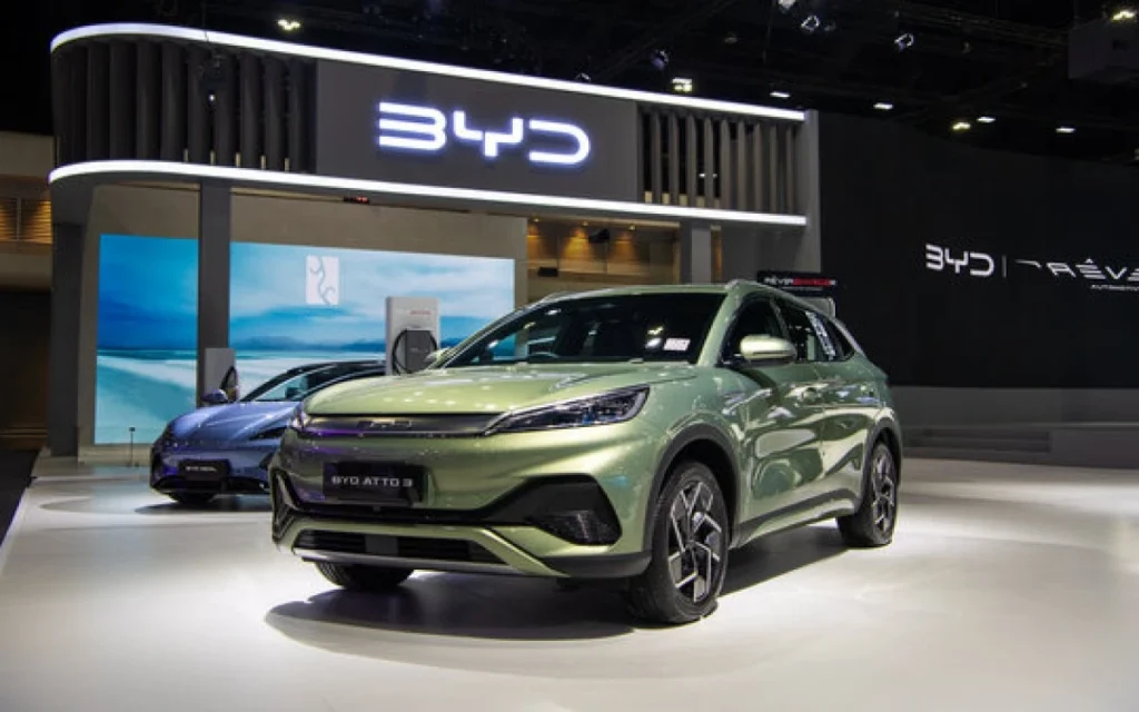 Carro da BYD me exposição. Há uma logomarca da empresa no alto. Falando sobre o seguro de carro elétrico byd.