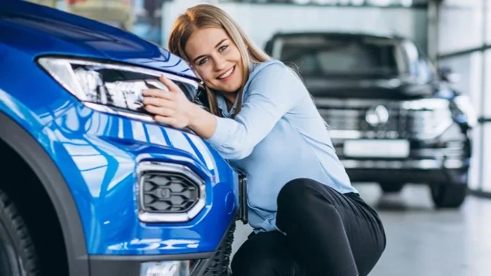 Mulher sorridente abraça veículo na cor azul. Falando sobre os tipos de cobertura de seguro auto.