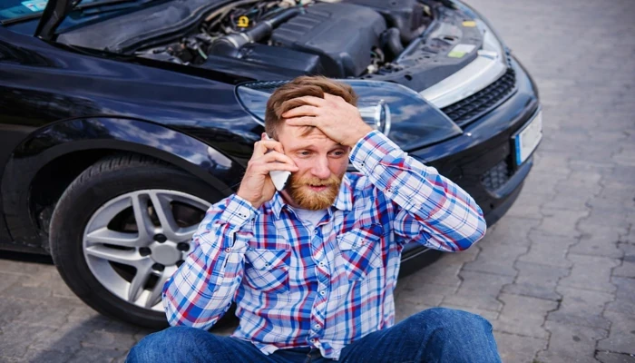 homem preocupado após acidente sem seguro falando ao telefone ao lado do carro danificado